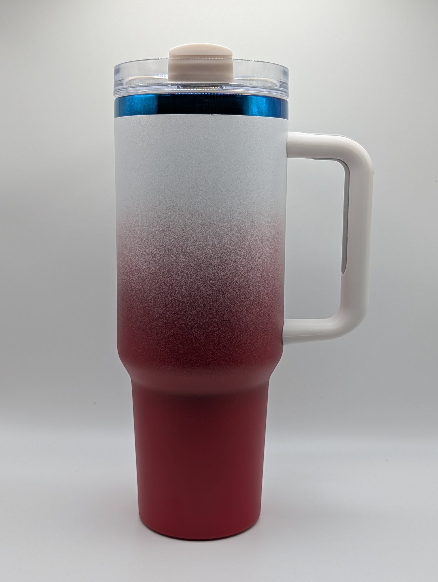 A travel tumbler with a frosted white to deep red gradient finish, featuring a white handle, a clear lid with a beige cap, and a blue accent ring near the top.